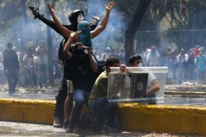 Anti-government protesters take cover with a shield stolen from the police during clashes with the police in Caracas